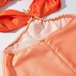 Nahaufnahme des eleganten orangefarbenen Satinkleids mit Raffung und metallischen Details.