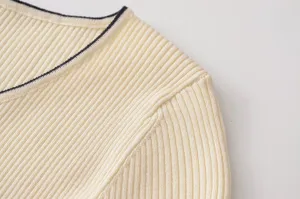 Primer plano detallado del cuello del jersey de punto crema con ribete oscuro y textura de canalé.