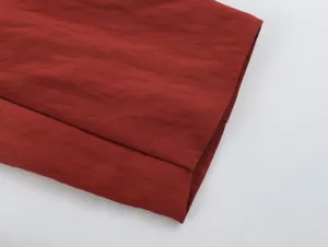 Close-up detail shot of dark red fabric hem with clean stitching and fine woven texture.