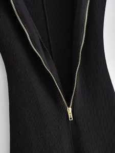 Close-up detail of black ribbed knit fabric featuring a shiny gold front zipper closure.