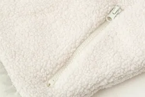 Primo piano dettagliato del tessuto del gilet in pile sherpa bianco e della sua cerniera.