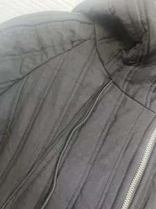 Black quilted winter jacket detail showcasing vertical stitching, hood and zipper design.