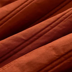 Close-up fabric detail of orange quilted winter coat, showing fine stitching lines and texture.