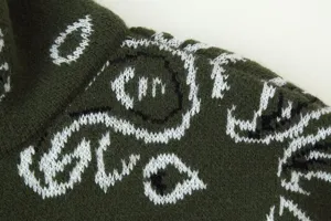 Close up of dark green knitted cardigan fabric with white jacquard abstract pattern texture