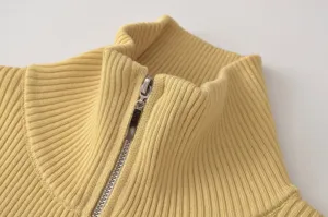 Detalle de jersey de punto acanalado con cuello alto y cremallera, textura amarilla suave.