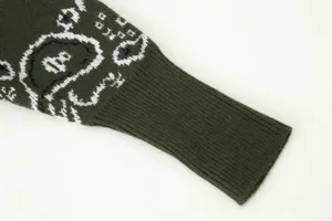 Detailed view of the dark green knitted sweater sleeve with white knit cartoon pattern.
