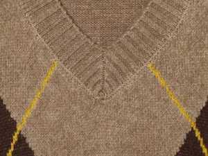 Dettaglio ravvicinato di maglione da donna con scollo a V e classico motivo a rombi.