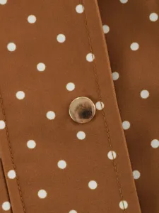Close-up detail of brown trench coat fabric with white polka dots and stylish metal snap button.
