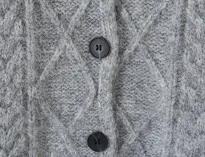 Close-up view van de grijze kabeltrui cardigan tricot textuur met zwarte knoppen detail.