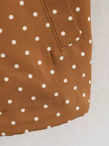 Brown polka dot trench coat fabric detail with pocket flap and stitching, elegant commuting style.