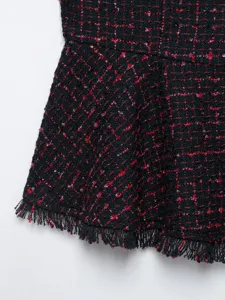 Dettaglio giacca smanicata in tweed nero e rosso con filo metallico e orlo con frange.