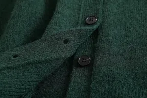 Close-up detail of dark green knit cardigan showcasing soft fuzzy texture and black button.