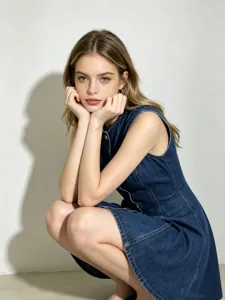Robe courte en jean bleu sans manches pour femme, col rond et boutons métalliques.