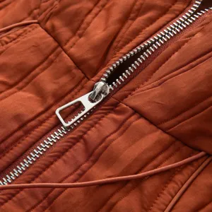 Close-up detail shot of a stylish rust orange quilted winter coat with silver metallic zipper.