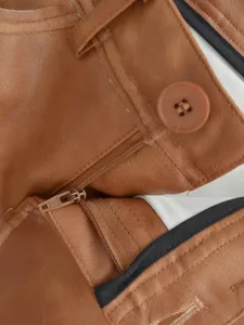 Close-up detail of brown PU leather skirt waistband, featuring zipper and button design.