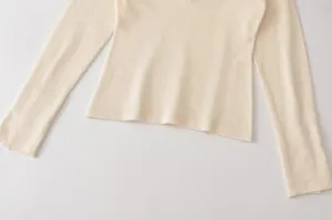 Nahaufnahme der feinen Stricktextur und des gerippten Bündchens am cremeweißen Oberteil.