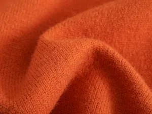 Detailaufnahme eines weichen orangen Strickpullover-Stoffes mit feiner Textur und gemütlichen Falten.