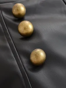 Close-up detail of high-waisted black leather shorts featuring vintage gold-tone metal dome buttons.