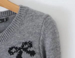 Detail view of gray knitted long-sleeve sweater featuring a classic black bow jacquard design.