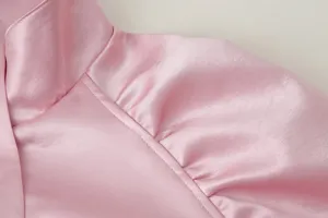 Detailaufnahme des eleganten rosa Satinoberteils mit feinem Stehkragen und Raffungen.