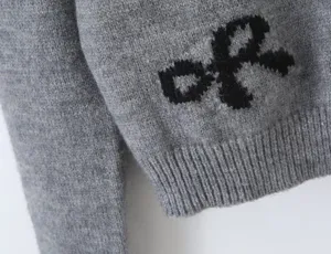 Grey knitted sweater detail with black bow pattern, soft texture, stylish casual winter apparel.