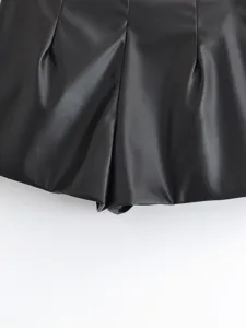 Close-up detail of black faux leather high waist pleated shorts texture and fold design