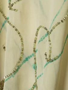 Detailed close-up of women's fashion top fabric with green print and sequin embroidery.