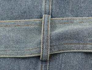 Close-up detail van de spijkerjas riemlus, duurzame denim stof met oranje stiksels.