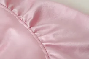 Nahaufnahme von rosafarbenem Satin mit Raffungen und feinen Nähten, weiche Textur.