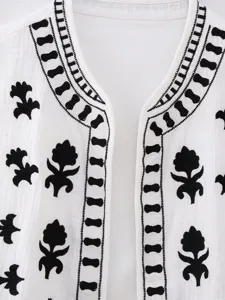 Detail view of the open-front vest featuring delicate black embroidery on white fabric.