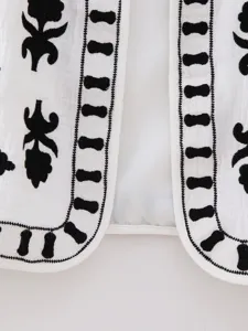 Exquisite close-up detail showcasing white fabric with black floral embroidery trim.