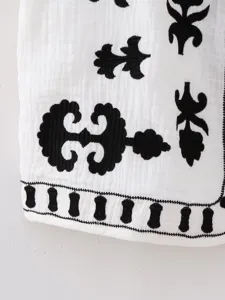 Close-up detail of embroidered white vest fabric showing intricate black patterns and texture.