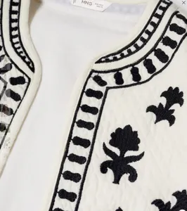 Detailed shot of a stylish white embroidered open front vest featuring intricate black patterns.