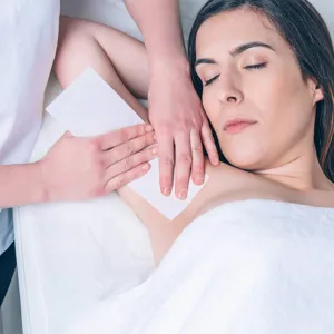 Close-up scene of professional underarm waxing treatment using soft disposable paper strips.
