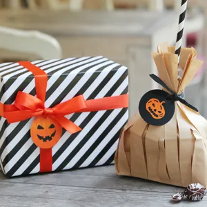 Λεπτομέρεια συσκευασίας δώρου halloween με ριγέ κουτί και χαριτωμένες ετικέτες κολοκύθας.