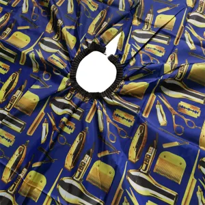 Detailed view of adult hairdressing cape with barber tools pattern and elastic neck band.