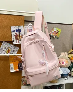 Pink canvas casual backpack detail view with front zipper pocket and cute heart charm hanging.