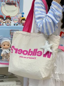 Detail shot of the canvas tote bag with pink straps, star charm, and bold printed lettering.