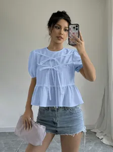 Detailed shot of light blue bow front peplum top and short sleeves in a clean indoor setting.