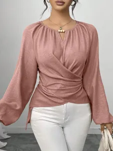 Nahaufnahme der eleganten Wickelbluse mit V-Ausschnitt, Perlendetail und unregelmäßigem Saum.