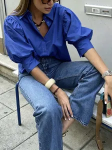 Close-up detail view of a chic blue puff sleeve button shirt worn in an outdoor street scene.