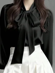 Close-up detail of the elegant black bow tie blouse, showing the smooth silk-like drape and collar.