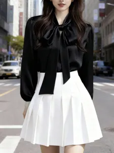 Detail shot of women's long sleeve bow tie satin blouse paired with white pleated skirt.