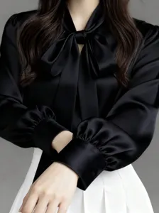 Close-up detail of black satin long sleeve blouse featuring elegant bow tie and cuffs.