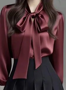 Close up detail of elegant wine red satin blouse with oversized bow tie collar and long sleeves.