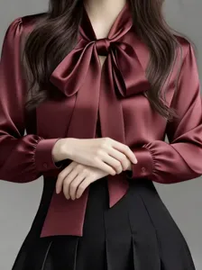 Close-up of elegant burgundy satin blouse with bow tie collar and pleated skirt detail.