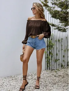Detail shot of brown off-the-shoulder long sleeve blouse worn by model outdoors on gravel.