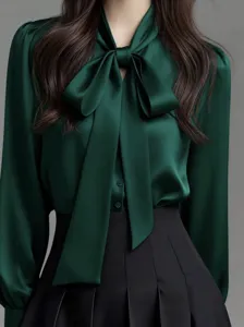 Detail view of elegant dark green satin blouse with bow tie collar and long sleeves.