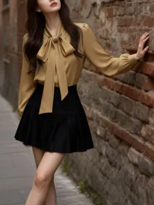 Close-up view of elegant bow tie collar and draped fabric on the camel long sleeve blouse.