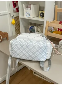 Sac à dos à carreaux bleu et blanc, tissu à pois et bretelles grises, posé sur une table